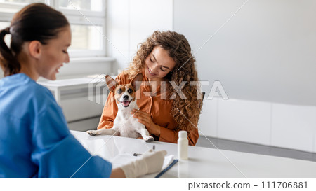 Curly-haired woman with her cheerful dog at vet consultation 111706881