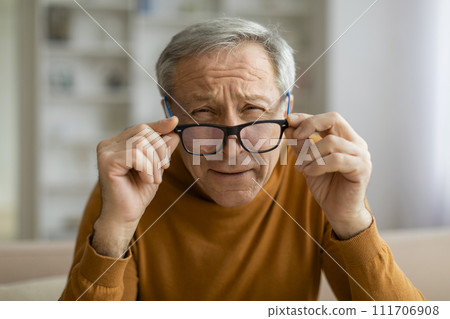 Tired elderly man removing eyeglasses, home interior 111706908
