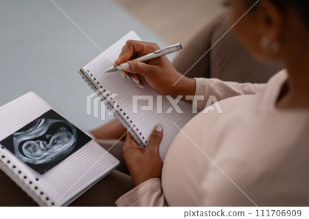 High angle view of black pregnant woman taking notes 111706909