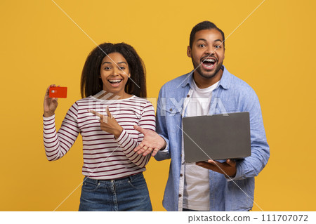 Online banking. Happy black couple using laptop and pointing at credit card 111707072