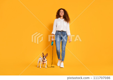 Smiling woman with her dog on leash against vibrant yellow backdrop 111707086