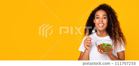 Black lady holding fresh salad in bowl on yellow background Black lady holding fresh salad in bowl on yellow background 111707258