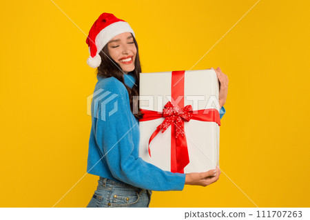 Joyful young woman holding wrapped Xmas gift on yellow background 111707263