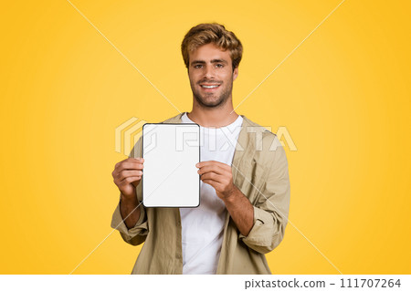 European man displays tablet with blank screen, yellow backdrop 111707264