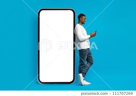 Young black guy in casual leaning against huge smartphone 111707269