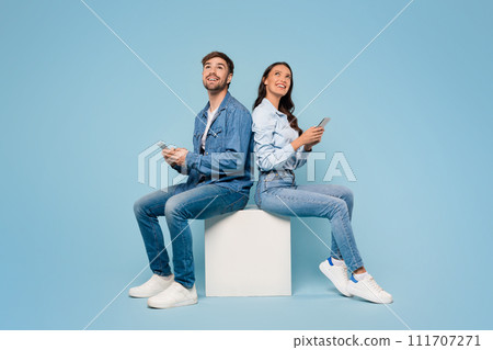 Spouses with mobiles gaze up, blue background 111707271