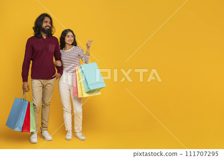 Cheerful millennial indian couple shopping together on yellow Cheerful millennial indian couple shopping together on yellow 111707295