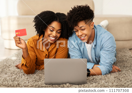 Cheerful young african american guy and woman shopaholics, use laptop 111707308