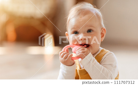 Closeup of cute little baby sitting on floor, chewing teether Closeup of cute little baby sitting on floor, chewing teether 111707312