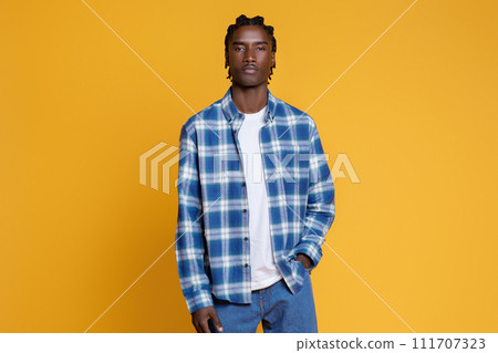 Stylish young black man wearing blue checkered shirt posing on yellow background 111707323
