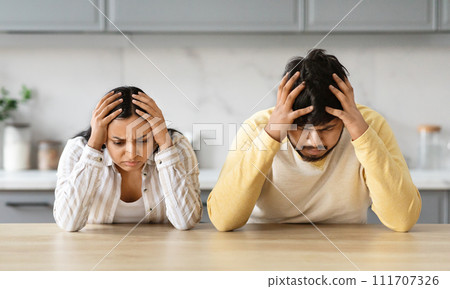 Sad couple with hands on head sitting in the kitchen Sad couple with hands on head sitting in the kitchen 111707326
