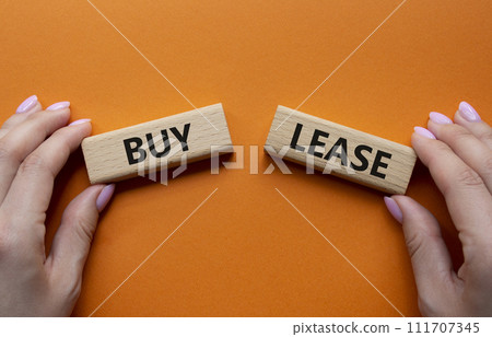 Buy or Lease symbol. Concept word Buy or Lease on wooden blocks. Businessman hand. Beautiful orange background. Business and Buy or Lease concept. Copy space 111707345