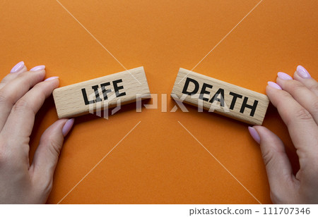 Life or Death symbol. Concept word Life or Death on wooden blocks. Businessman hand. Beautiful orange background. Business and Life or Death concept. Copy space 111707346