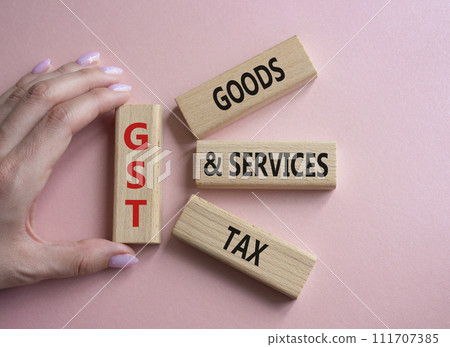 GST - Goods and Services Tax symbol. Concept word GST on wooden blocks. Businessman hand. Beautiful pink background. Business and GST concept. Copy space. 111707385