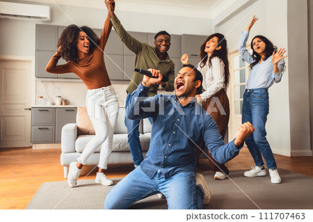 guy with microphone singing karaoke song while friends dancing indoors 111707463