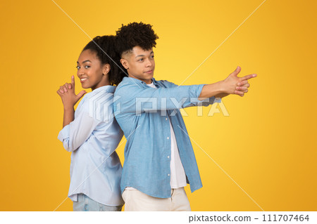 Two young African American individuals back to back, playfully gesturing imaginary guns Two young African American individuals back to back, playfully gesturing imaginary guns 111707464