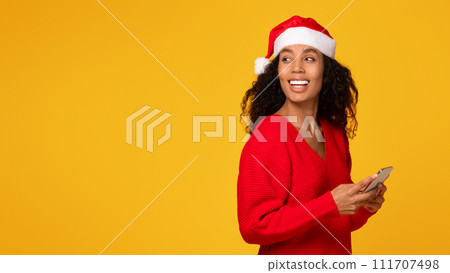 Black lady with cellphone in hands, woman wearing Santa hat, looking back at free space Black lady with cellphone in hands, woman wearing Santa hat, looking back at free space 111707498