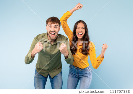 Ecstatic couple celebrating success with fists raised, blue background Ecstatic couple celebrating success with fists raised, blue background 111707588