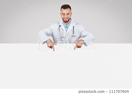 Male doc pointing at white placard, grey background 111707604
