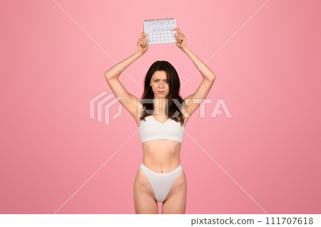 A determined young woman with a skeptical expression holds up an eye chart above her head 111707618