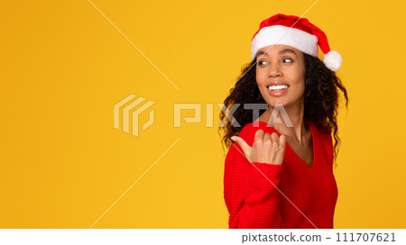 Lady in Santa hat pointing back at free space on yellow background Lady in Santa hat pointing back at free space on yellow background 111707621