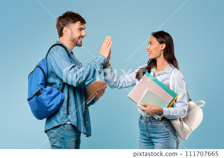 Happy male and female students high five with books, blue background Happy male and female students high five with books, blue background 111707665