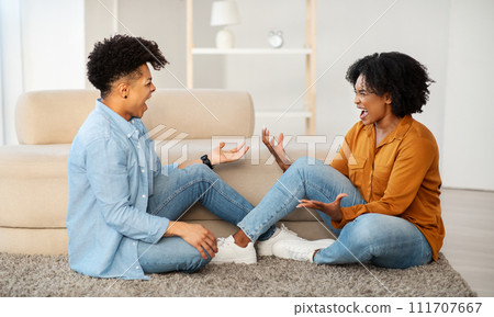 A sad young couple sits on the floor having a bad conversation, with expressive gestures 111707667