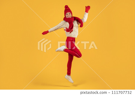 lady in winter clothes leaping with joy on yellow backdrop 111707732
