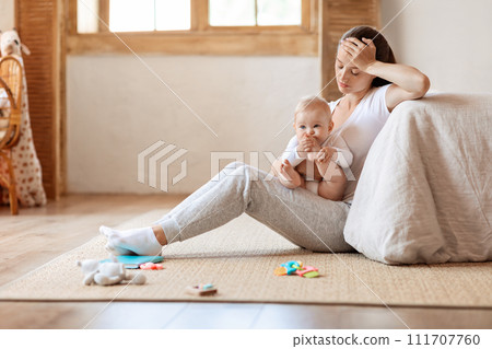 Depressed young woman sitting with cute baby boy on floor Depressed young woman sitting with cute baby boy on floor 111707760