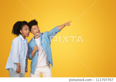 Excited African American young man pointing away with a thrilled expression as the young woman 111707767