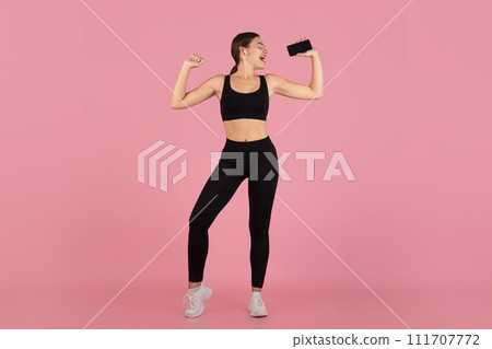 Joyful young woman in sportswear using her smartphone as microphone, passionately singing Joyful young woman in sportswear using her smartphone as microphone, passionately singing 111707772