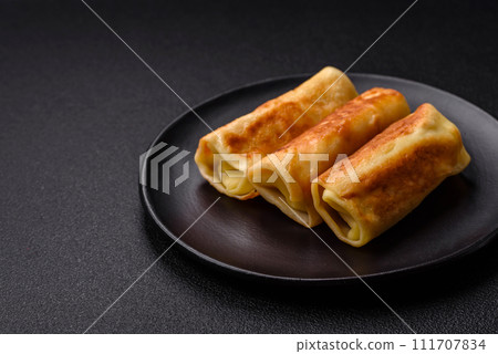 Delicious fried pancakes with filling rolled on a dark concrete background Delicious fried pancakes with filling rolled on a dark concrete background 111707834