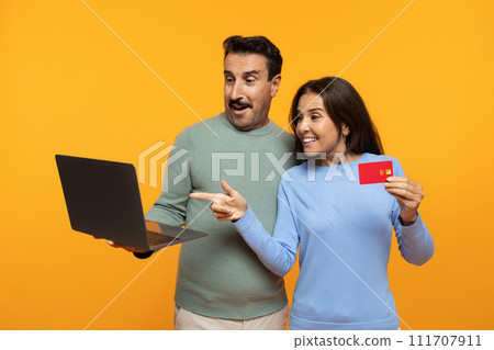 Happy excited senior european man and lady point finger at laptop, show credit card Happy excited senior european man and lady point finger at laptop, show credit card 111707911