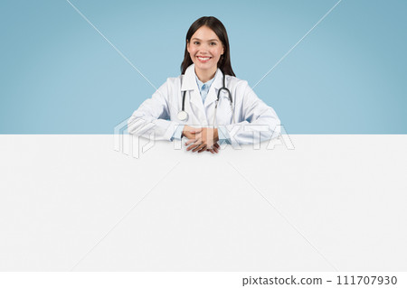 Cheerful woman doctor with ad board on blue backdrop, copy space Cheerful woman doctor with ad board on blue backdrop, copy space 111707930
