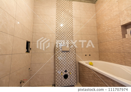 Unfinished reconstruction of bathroom or toilet with light beige geometric ceramic tiles installed on walls, place for lavatory and bath. Unfinished reconstruction of bathroom or toilet with light beige geometric ceramic tiles installed on walls, place for lavatory and bath. 111707974