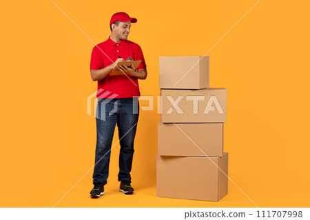 Arab courier with clipboard near stack of cardboard boxes, studio 111707998
