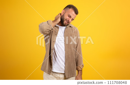Unhappy millennial european man with beard in casual massaging neck with hand, suffer from pain 111708048