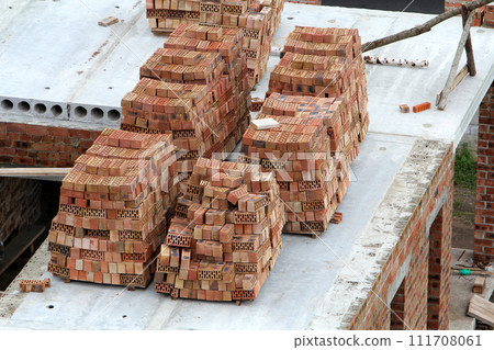 Neat stacks of red bricks lit by summer sun piled on basement floor of future house under construction. Masonry, bricklaying and high quality long lasting building materials concept. Neat stacks of red bricks lit by summer sun piled on basement floor of future house under construction. Masonry, bricklaying and high quality long lasting building materials concept. 111708061