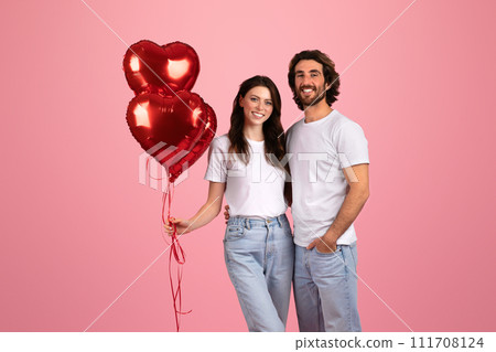 Content couple standing close, with the woman holding shiny red heart-shaped balloons Content couple standing close, with the woman holding shiny red heart-shaped balloons 111708124