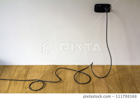Black electric cable in wall socket on wooden parquet floor Black electric cable in wall socket on wooden parquet floor 111708168
