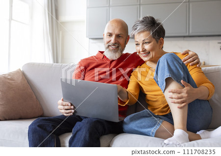 Smiling Senior Spouses Resting With Laptop In Living Room Interior Smiling Senior Spouses Resting With Laptop In Living Room Interior 111708235