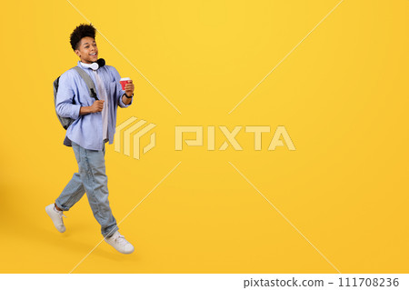 Happy male student walking with coffee on yellow background 111708236