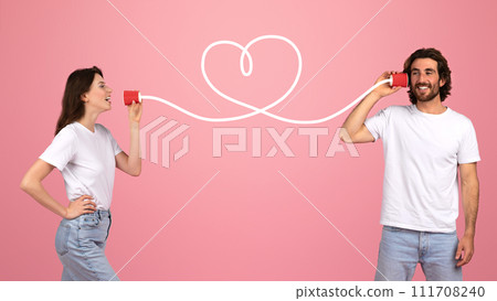 A young couple playfully communicates through tin can telephones connected A young couple playfully communicates through tin can telephones connected 111708240