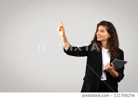 Happy young businesswoman in suit holding tablet and touching something invisible or interact with virtual interface 111708256