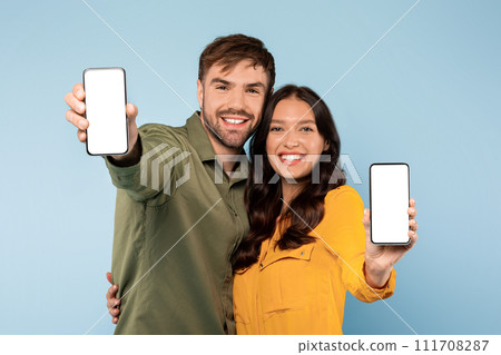 Joyful couple showing blank smartphone screens, blue backdrop Joyful couple showing blank smartphone screens, blue backdrop 111708287