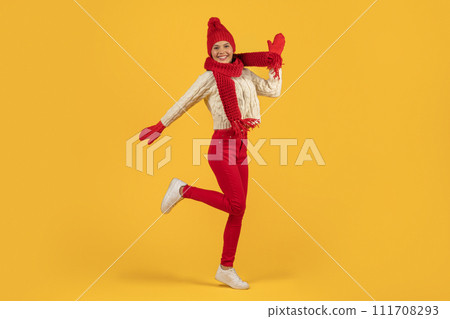 Joyful woman in red knitted hat jumping on yellow backdrop 111708293