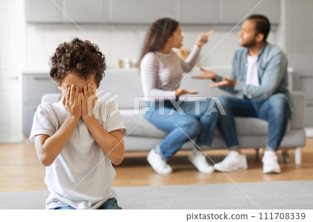Upset black preteen boy covering face with hands while his parents arguing Upset black preteen boy covering face with hands while his parents arguing 111708339