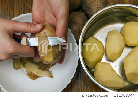 Detail of woman hands peeling fresh yellow potato with kitchen knife, Food preparation concept. Detail of woman hands peeling fresh yellow potato with kitchen knife, Food preparation concept. 111708344