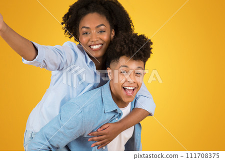 Exuberant young woman with arms wide open riding piggyback on a delighted young man Exuberant young woman with arms wide open riding piggyback on a delighted young man 111708375