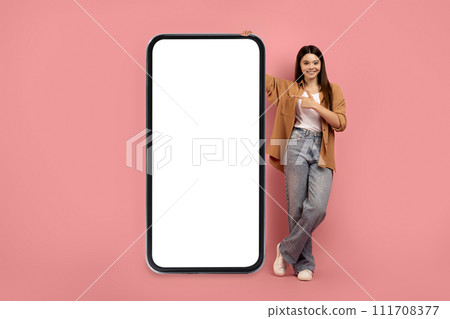 Smiling Teen Girl Pointing At Big Smartphone With Blank White Screen Smiling Teen Girl Pointing At Big Smartphone With Blank White Screen 111708377